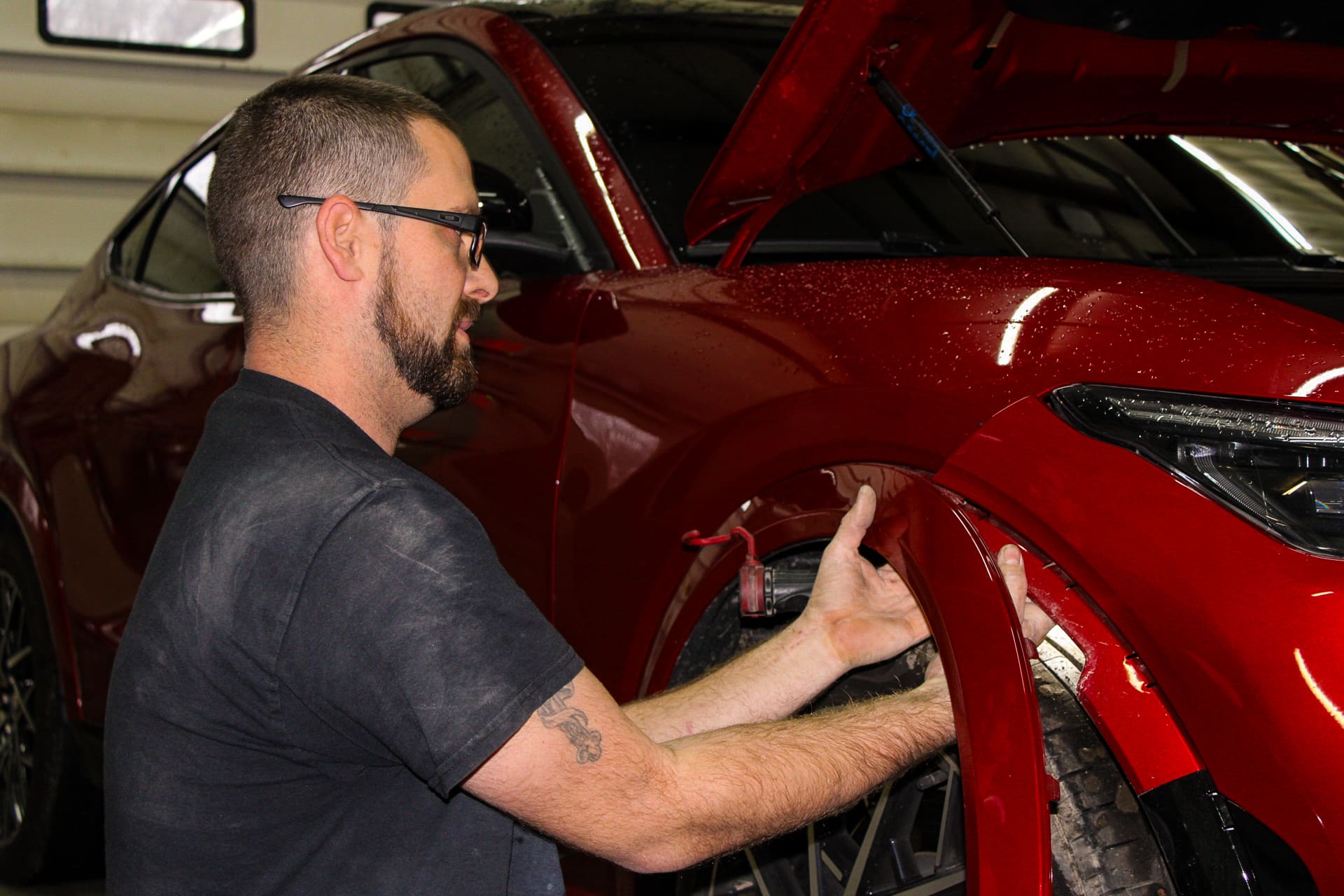 Adam from Evolve Auto servicing the fender of a red car. Adam can be seen placing a new fender over top of the car's left front tire.